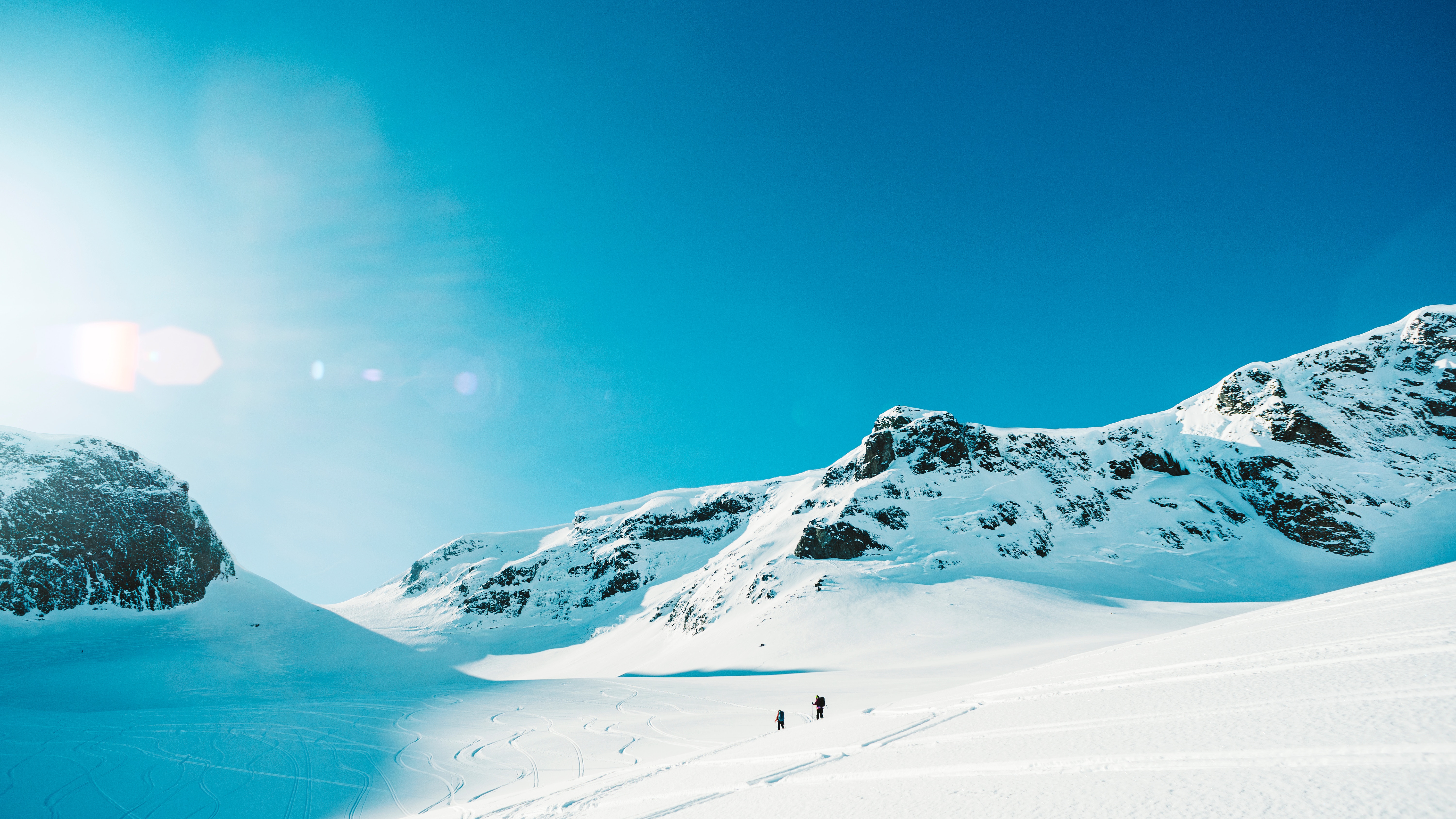 Two people in the distance crossing a snowy mountainous landscape