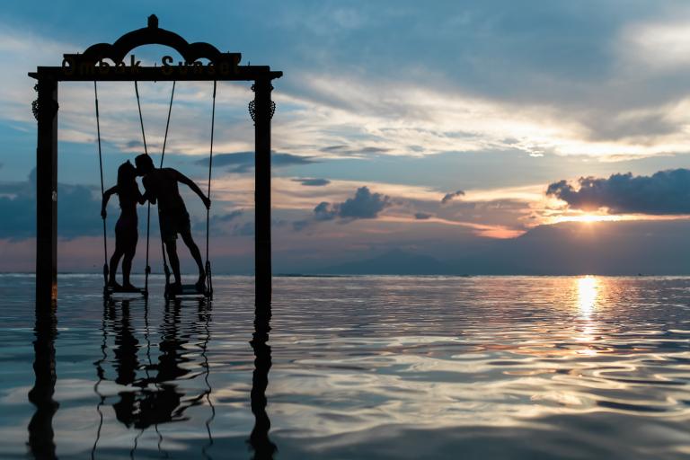 Silhouette of a couple holding hands and kissing while suspended above water