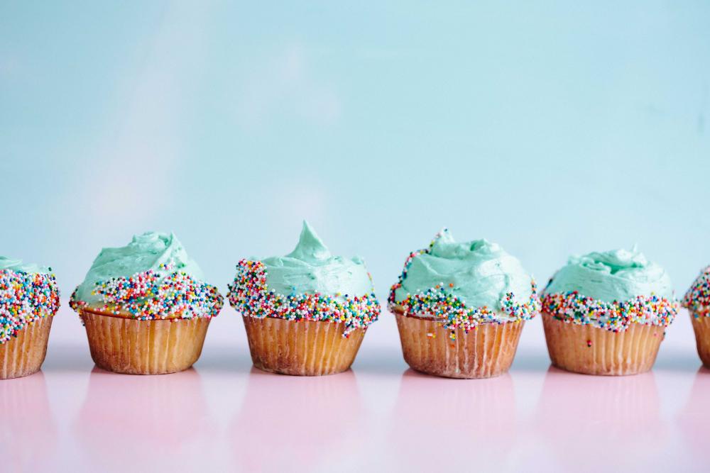 A row of frosted cupcakes on a table against a pastel blue wall