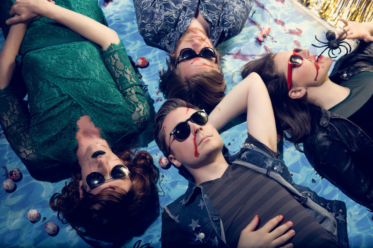 The members of Dalton Deschain and the Traveling Show lying on a picnic blanket covered in fake blood