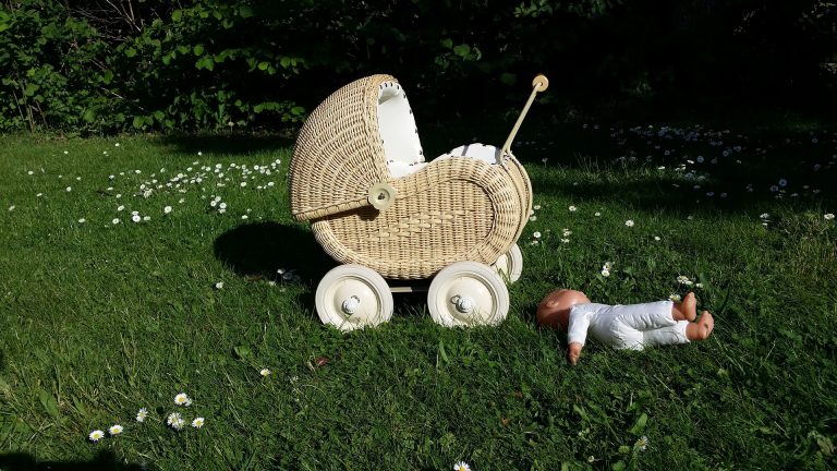 A wicker pram and baby doll lying in the grass