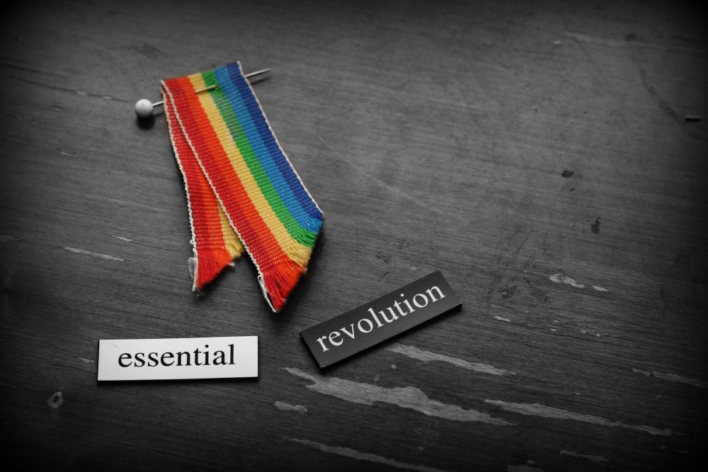 Rainbow ribbon and two magnetic poetry tiles reading "essential revolution"