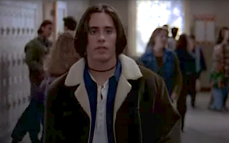 Jared Leto as Jordan Catalano. He is a young white man with chin-length hair wearing a choker necklace, layered shirts, and a jacket with a sheepskin collar