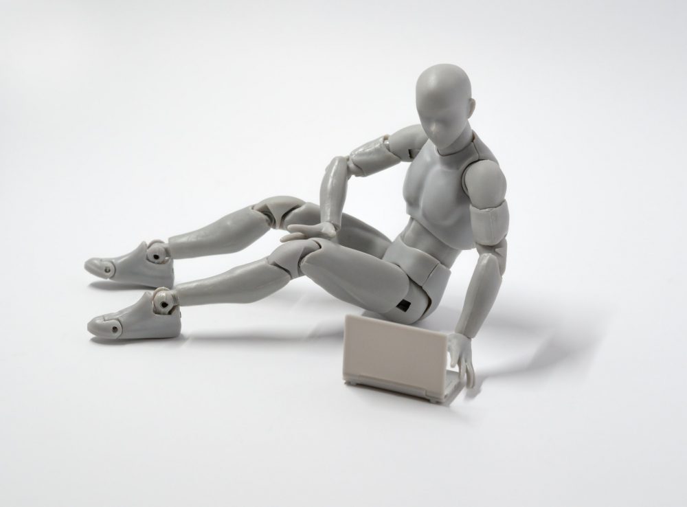 Humanoid silver figure with articulated joints typing on a laptop