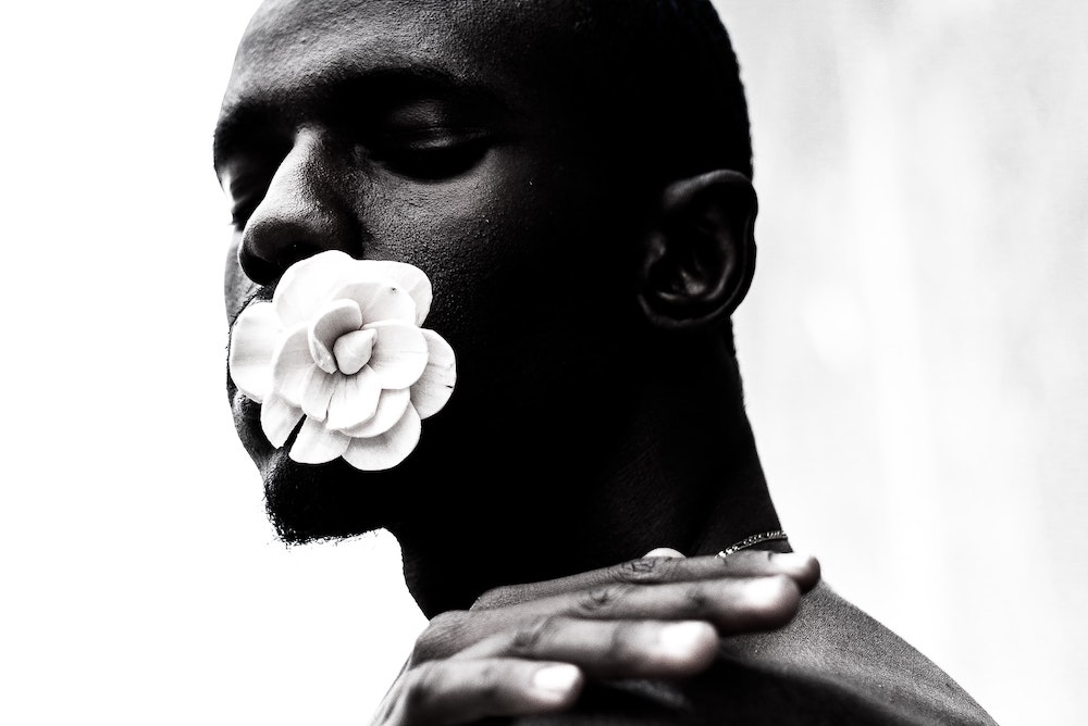 Black and white photograph of dark-skinned man with a white flower at his mouth