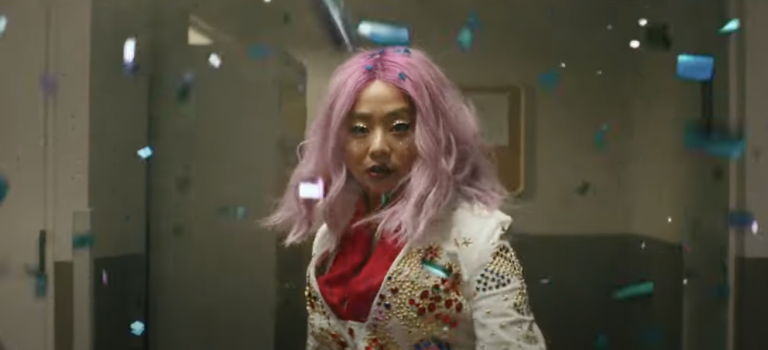 Femme wearing sparkly jacket with pink hair surrounded by blue confetti.
