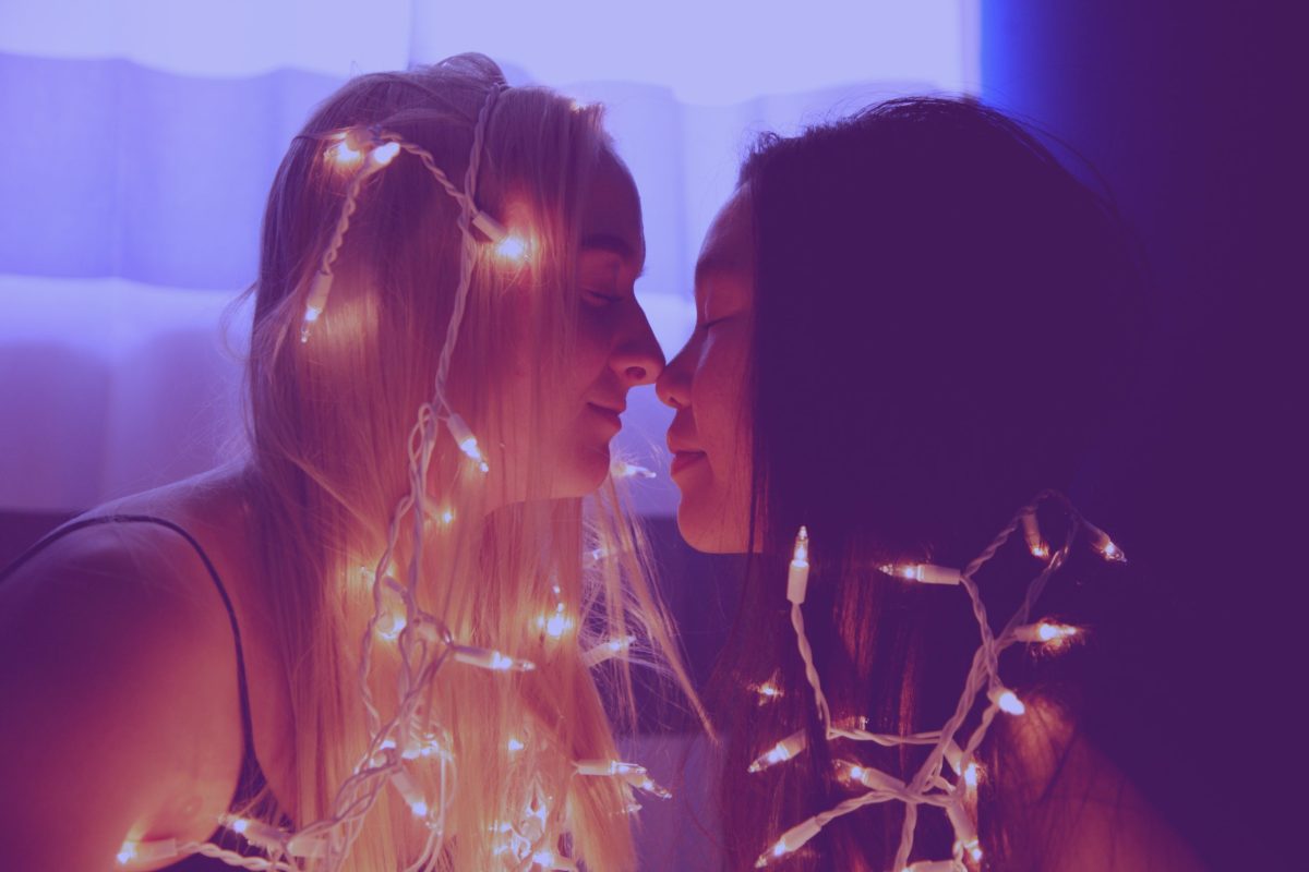 Two women sitting closely covered in fairy lights