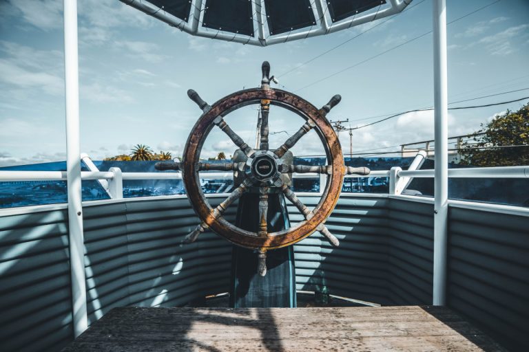 A steering wheel at the front of the ship on a bright day, overlooking the ocean.
