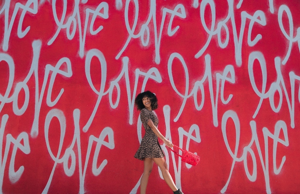 Person walking in front of a red wall covered in cursive graffiti reading 'love'