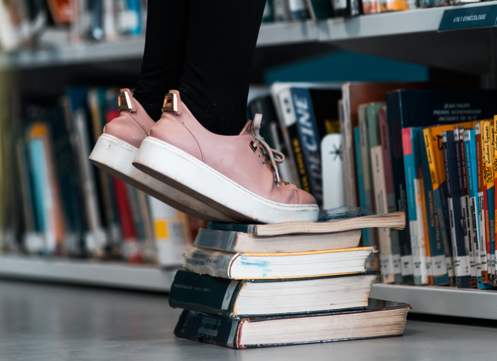 Person wearing pink sneakers stands on a stack books.