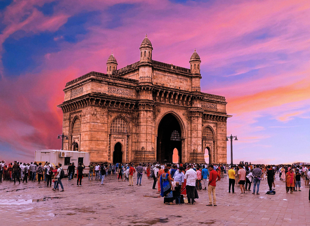 A large group of people admire the Gateway of India in Mumbai as the sun sets.