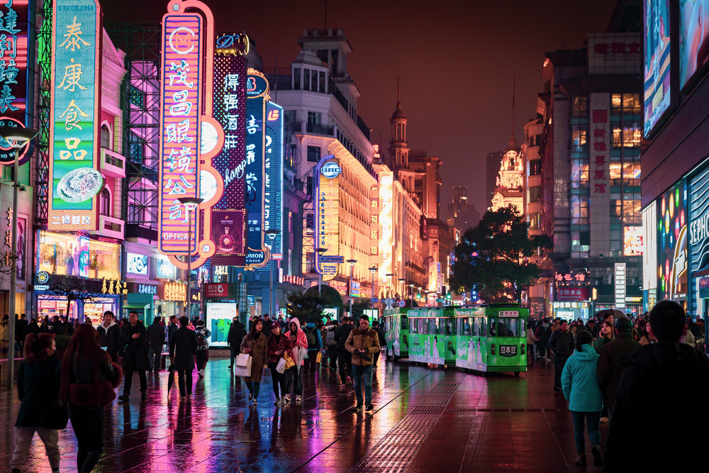 People walk down a busy street lit with neon in Shanghai.