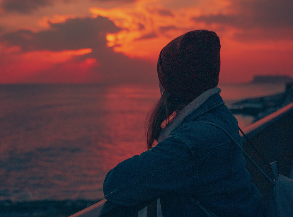 A woman in a beanie gazes at the sunset