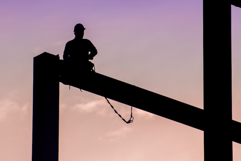 Silhouette of a construction worker sitting on a beam against the pale dawn