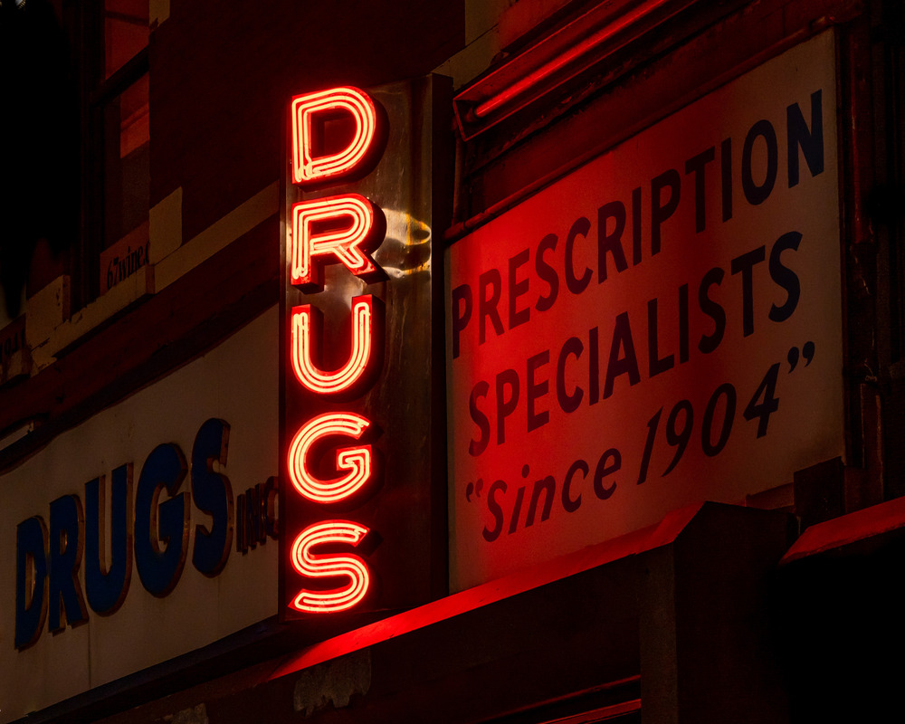 A red neon sign advertising "drugs" attached to a pharmacy.