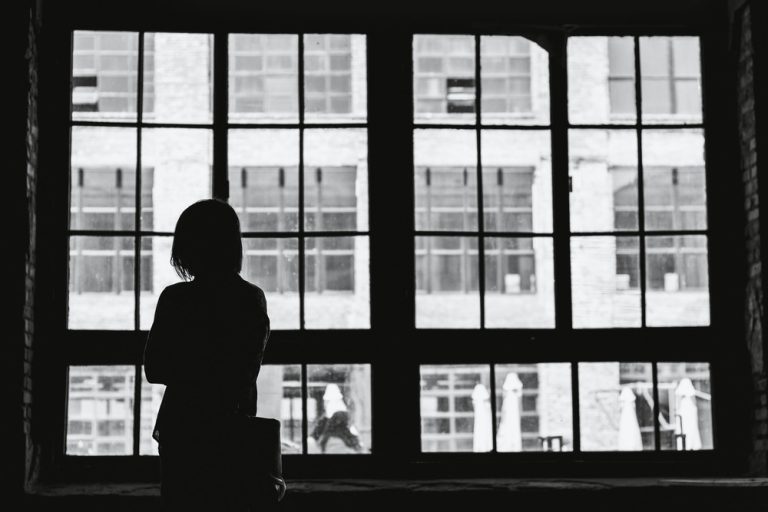 A black and white photo of a woman staring out a window