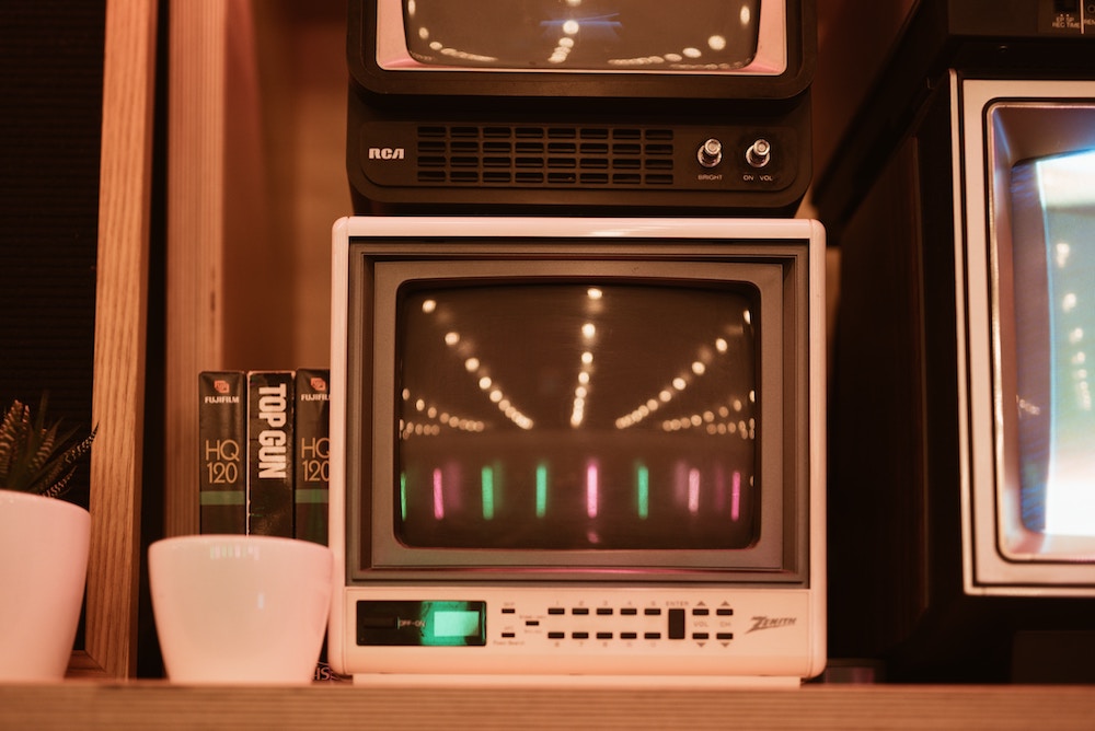 Vintage televisions stacked on top of one another, reflecting red, green, and white lights