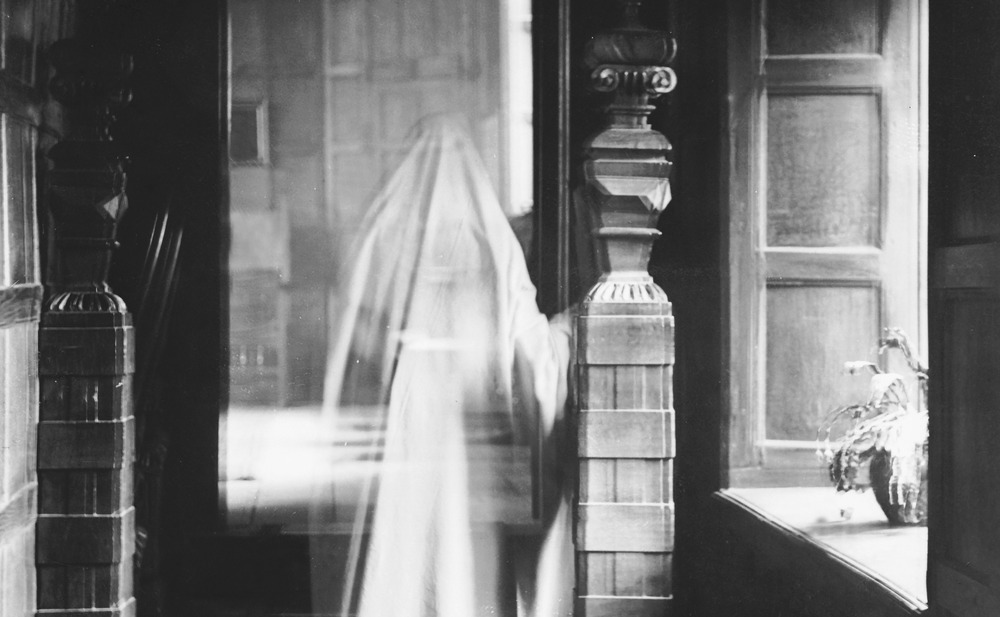 A double exposed image of a ghost standing alone in a room