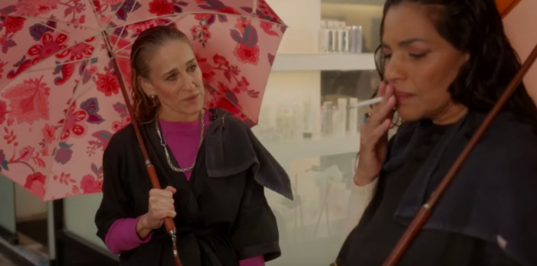 Seema and Carrie from “And Just Like That” standing in the rain with umbrellas