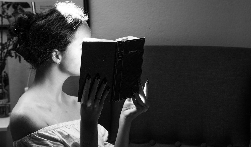 A woman sits in a chair and reads a book, her face obscured