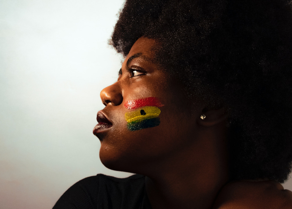 A woman with the Ghanaian flag painted on her cheek looks off to the side