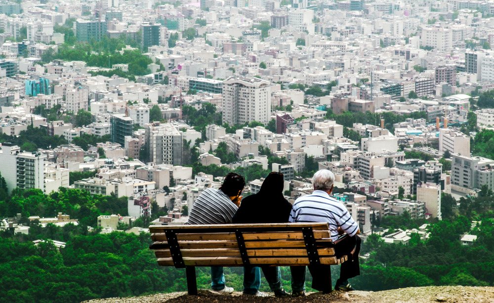 Three people sitting on a bench overlooking the city in Tehran, Iran