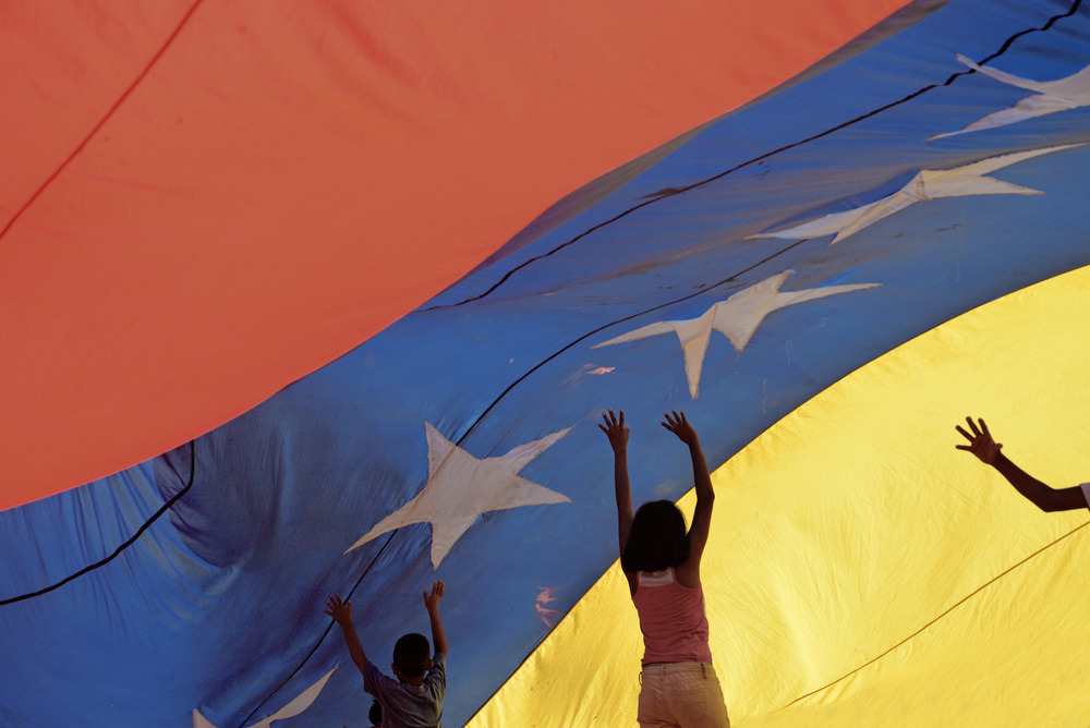 Three children play under a large Venezuelan flag