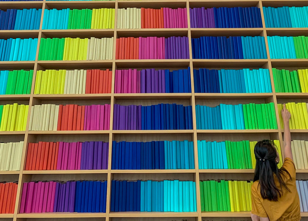 A woman stands in front of a multi-colored bookcase