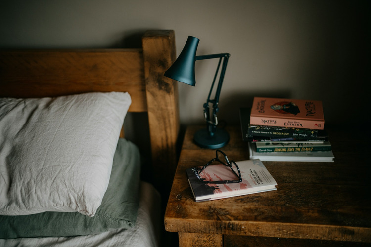 A stack of books on a bedside table near a lamp.