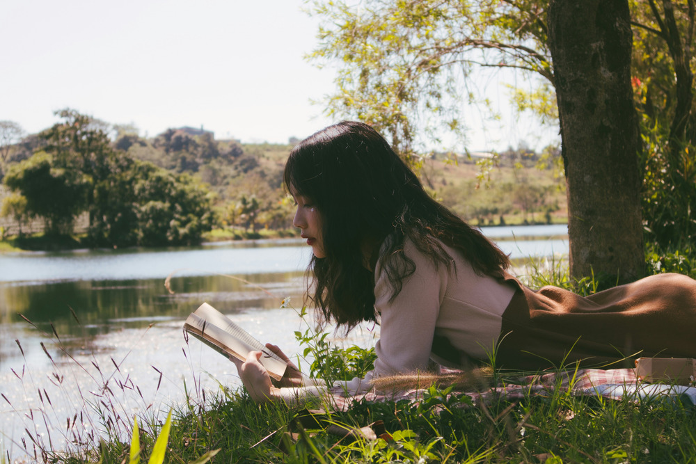 A young woman sits in the grass reading a book