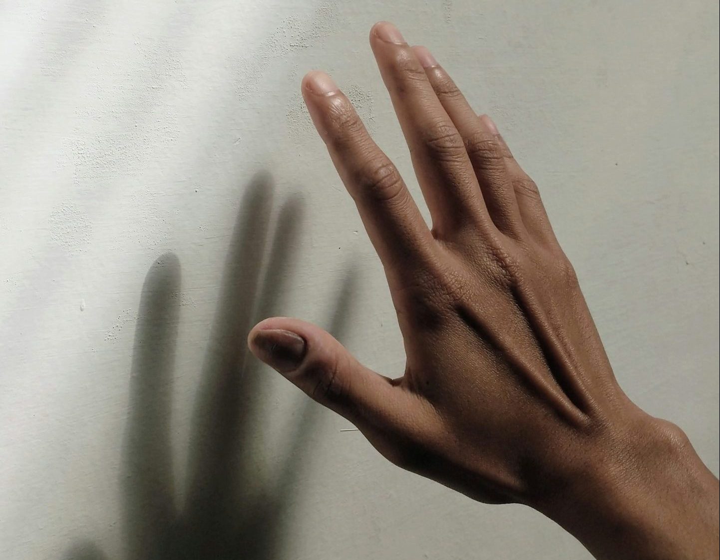 A medium-toned hand reaches toward a white wall